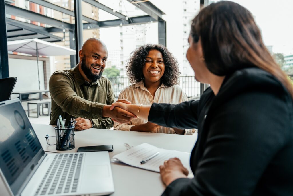 Smiling couple finalizing a deal with a business advisor—illustrating a successful process to buy a business or invest in businesses for sale.